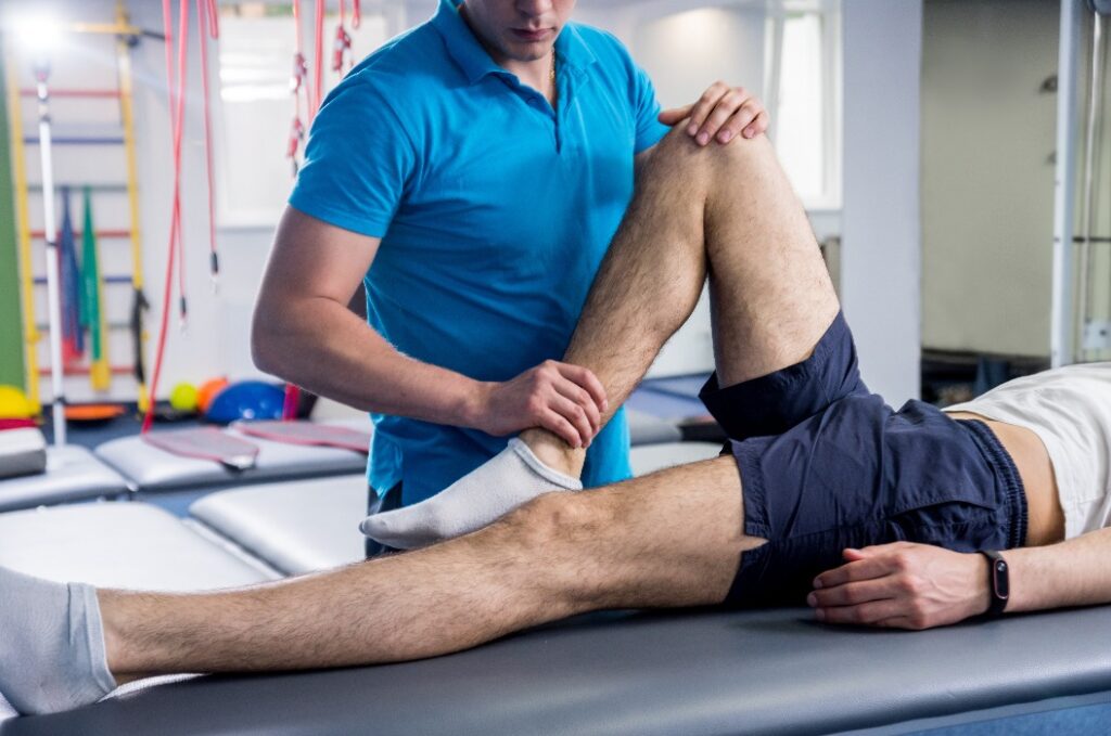 Rehabilitationstherapie. Physiotherapeutin bei der Arbeit mit einem jungen männlichen Patienten im Rehabilitationszentrum