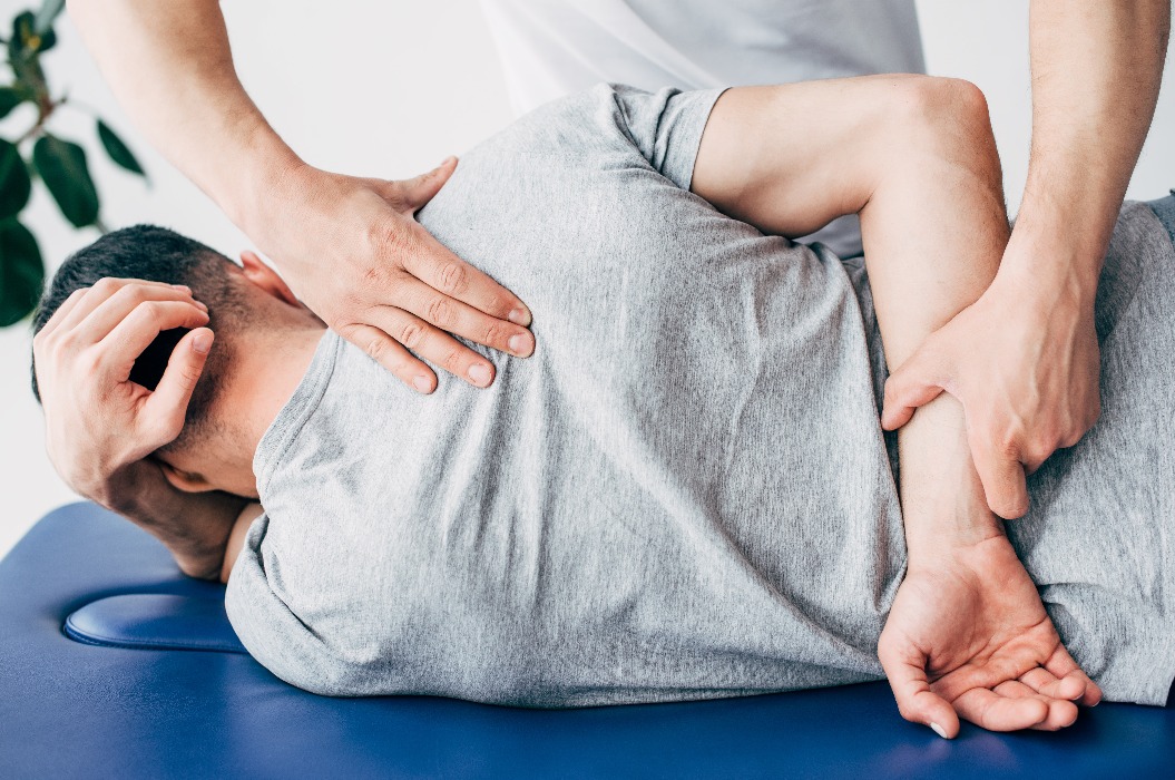 Rückenansicht eines Chiropraktikers, der den Rücken eines Mannes massiert, der auf einem Massagetisch im Krankenhaus liegt